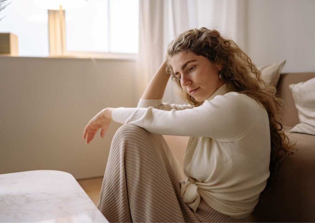 A woman sitting alone at home, looking sad and lonely as she reflects quietly.