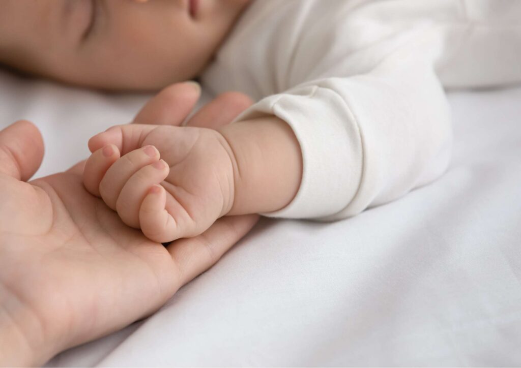 A close‑up of a mother gently holding her baby’s tiny hand, with the baby’s fingers wrapped around hers. A soft, intimate moment showing early bonding.