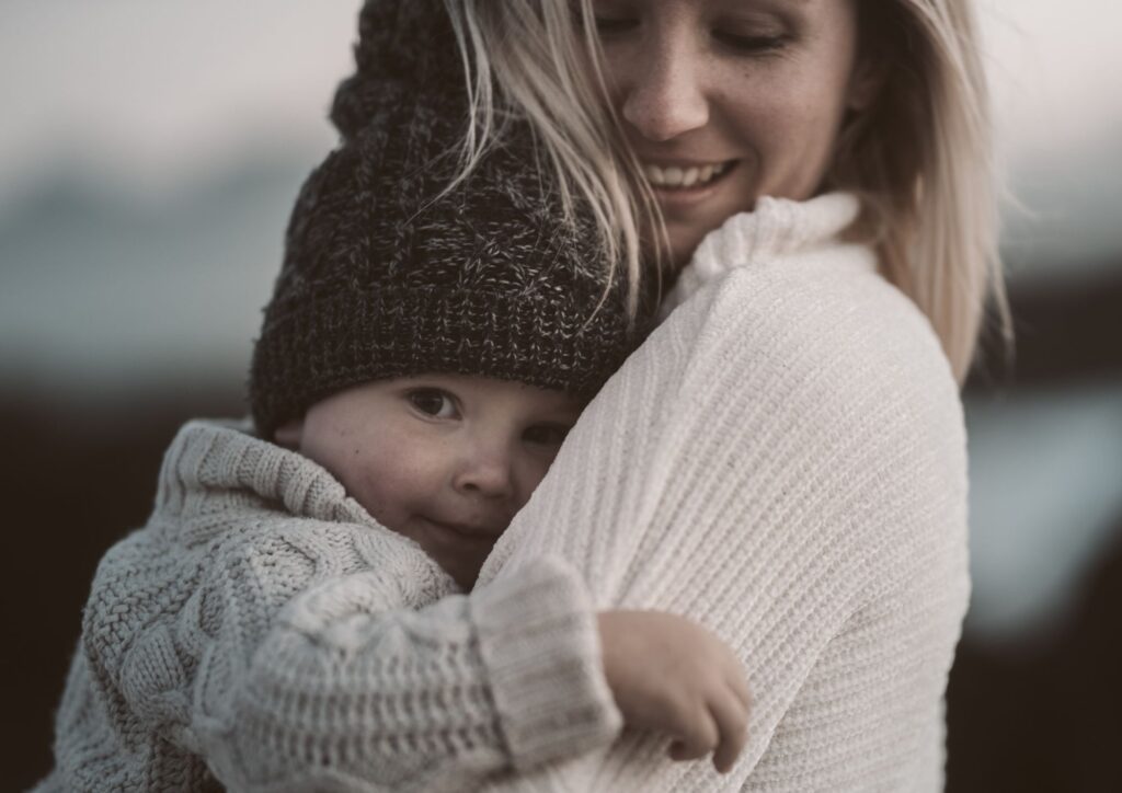 A parent holding a toddler close in a warm outdoor setting, expressing emotional safety and closeness.