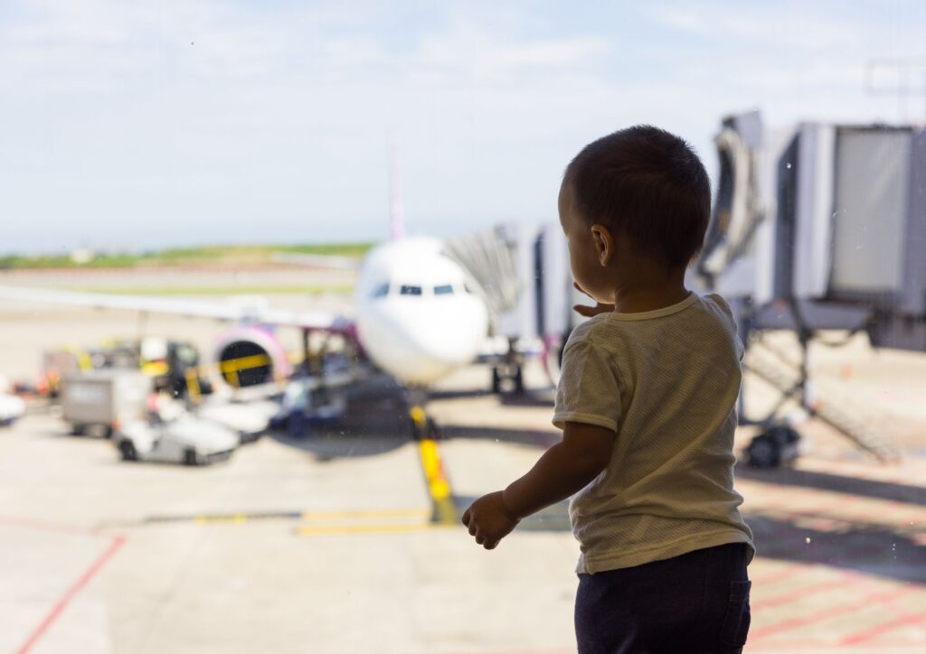 A toddler standing at an airport window looking at an airplane parked at the gate during a layover.