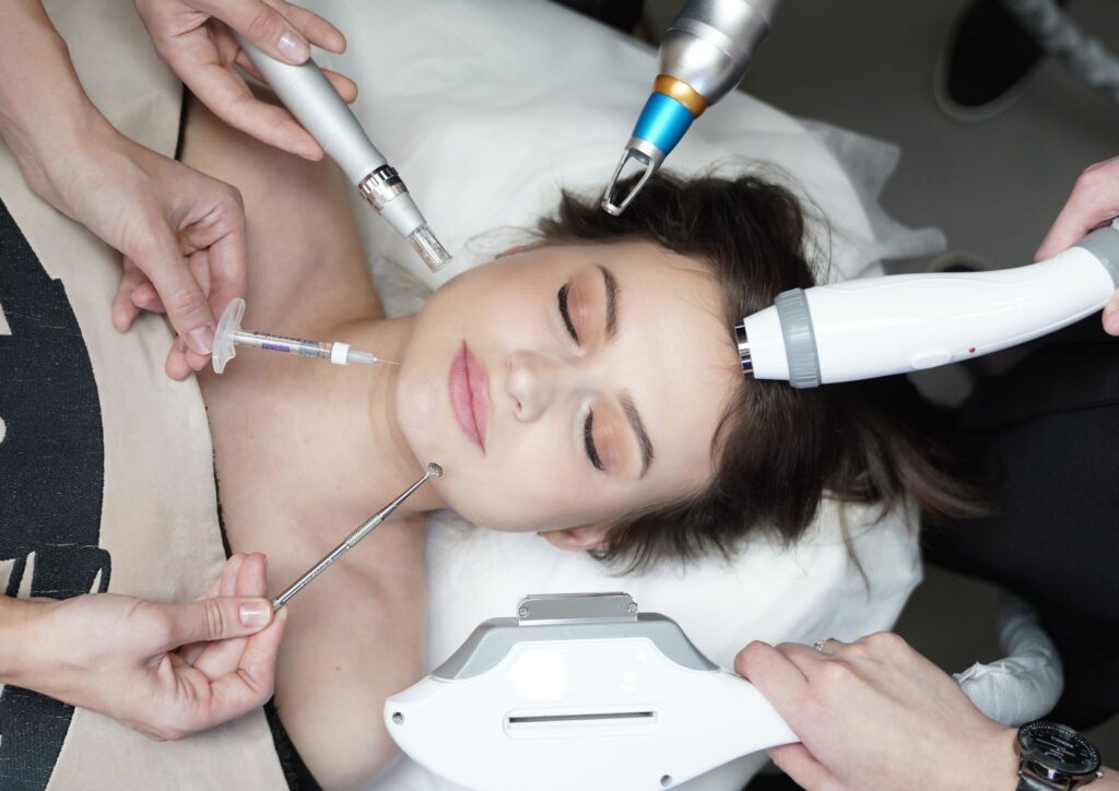 Multiple aesthetic tools and a syringe being used around a person’s face during a cosmetic procedure.