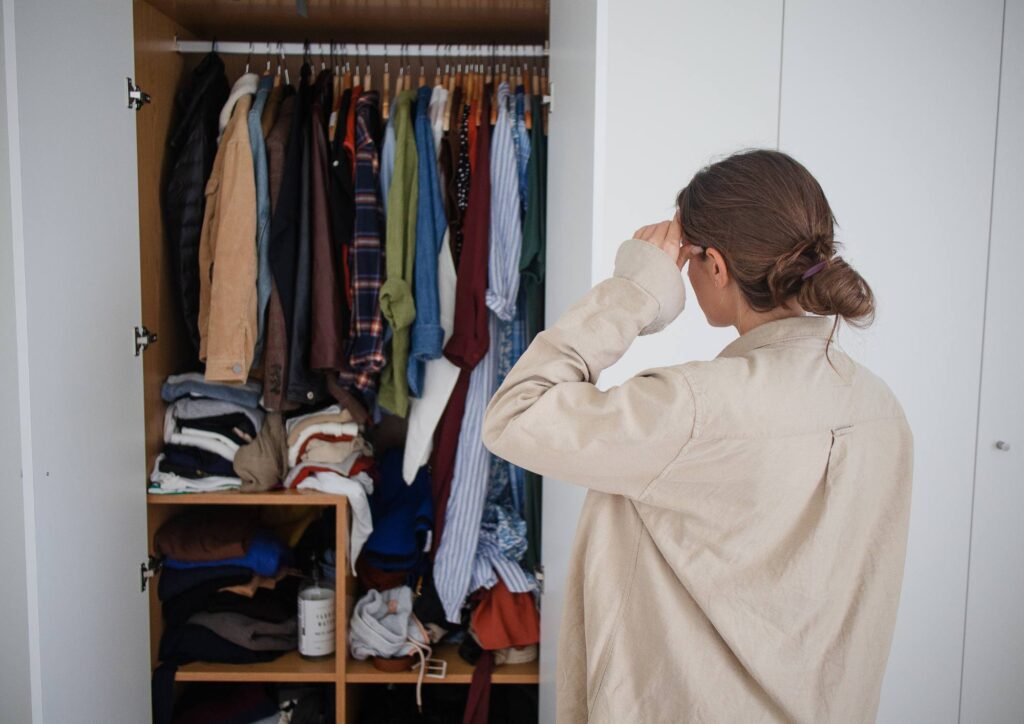 A woman standing in front of an open wardrobe filled with clothes, deciding what to wear.