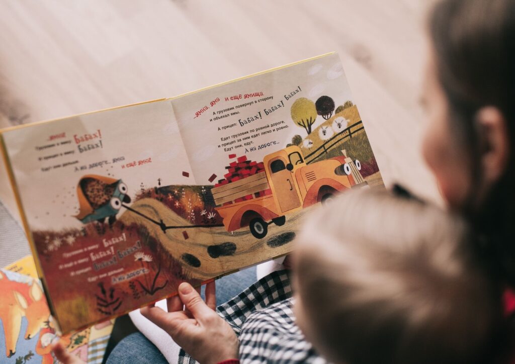An adult and toddler reading a colorful children’s book together, highlighting connection, communication, and shared routines.