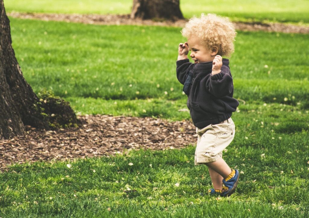A toddler running across a grassy park, showing the wobbly, joyful transition from walking to confident running.