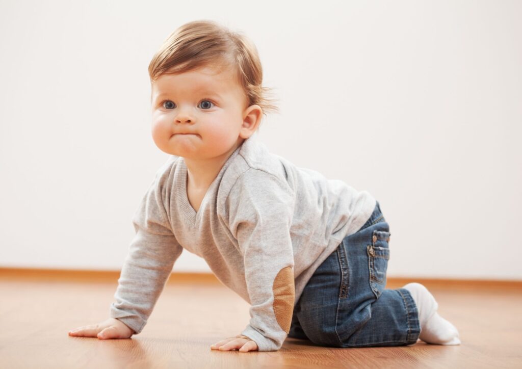 A toddler crawling across a wooden floor, capturing the commando‑crawl stage and early movement independence.