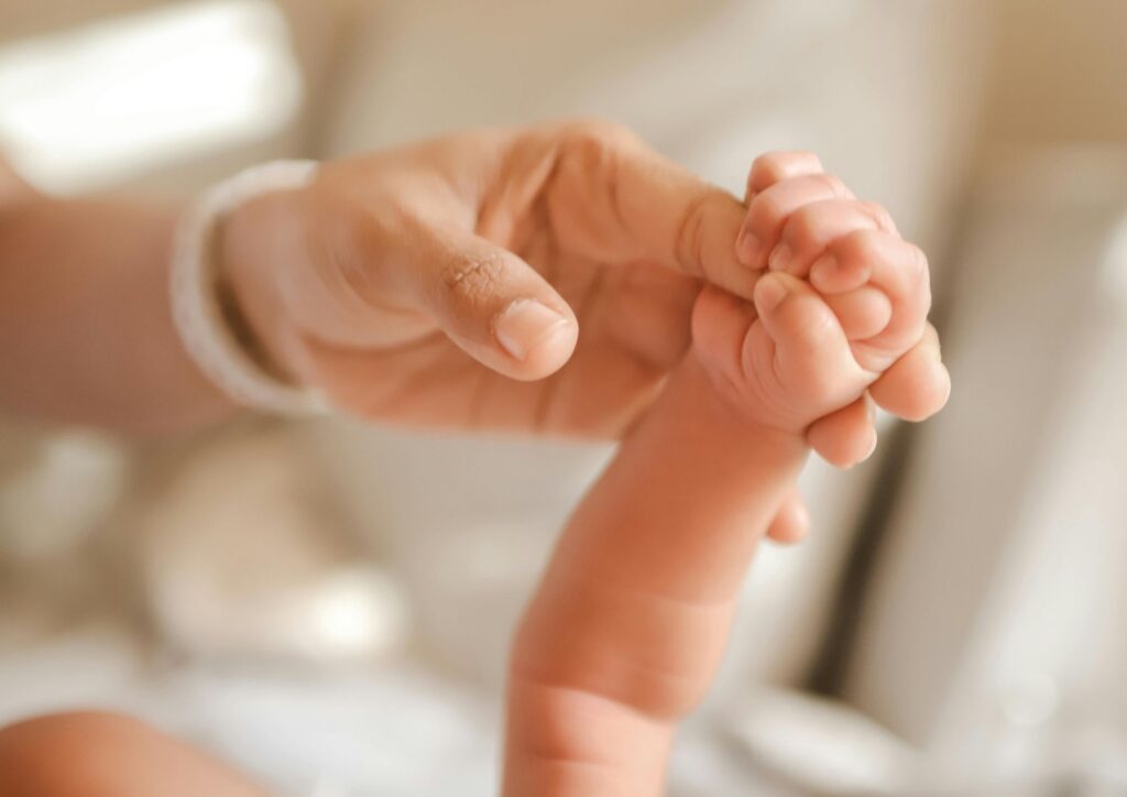 A tiny newborn hand wrapped around an adult’s finger, symbolizing vulnerability and the protective bond of early motherhood.
