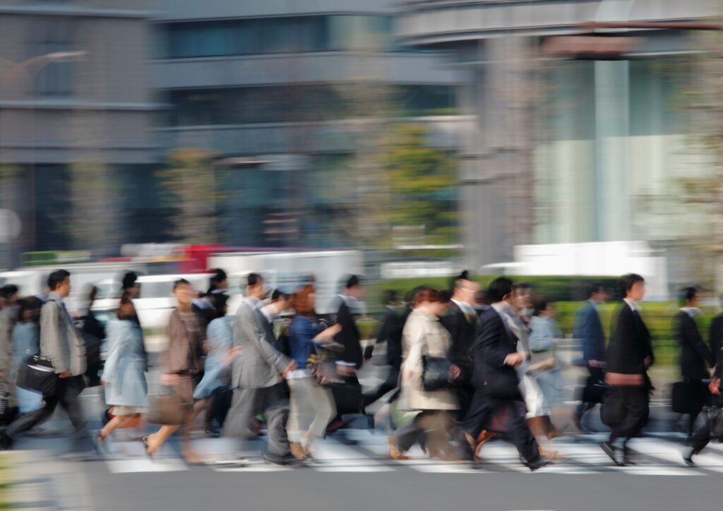 A crowded city crosswalk filled with people in business attire rushing in different directions, symbolising the fast‑paced pressure of modern work life.