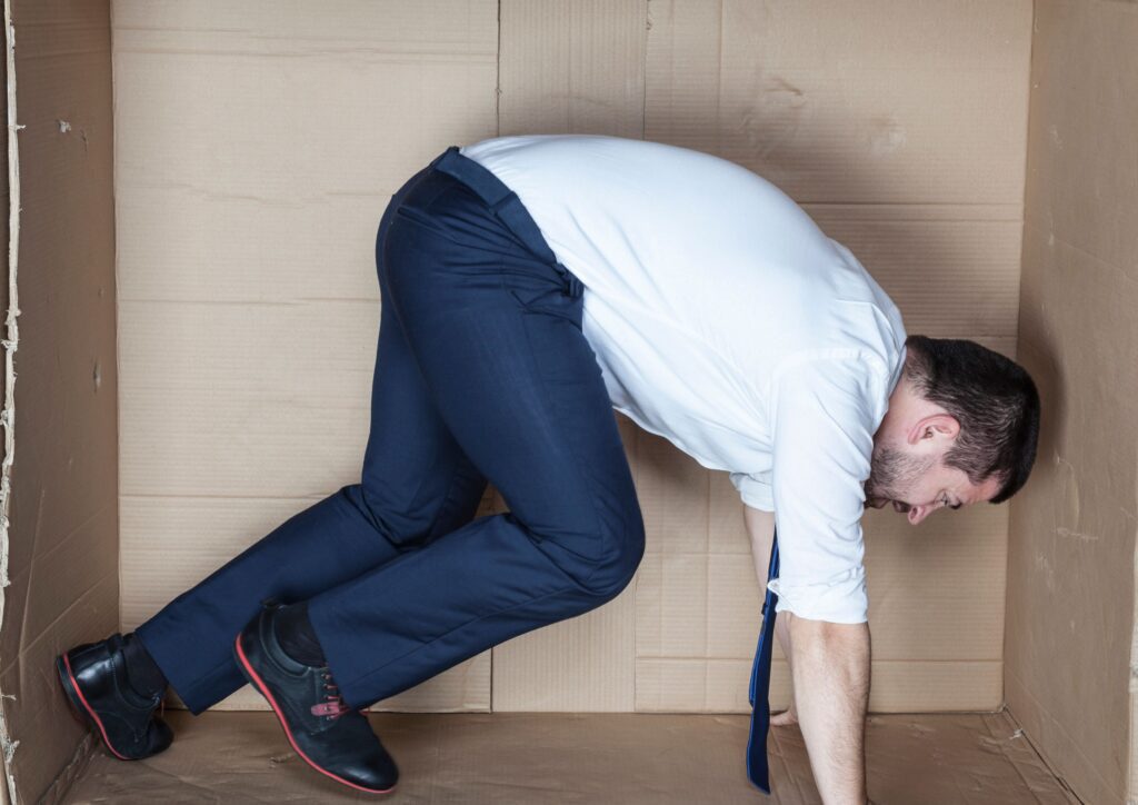 A person in business clothes squeezed inside a small cardboard box, visually expressing the feeling of being trapped or restricted in a job.