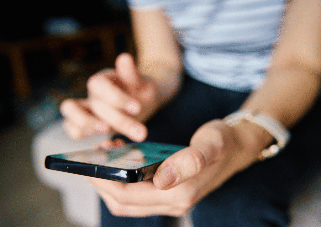 A close-up of hands holding a smartphone, scrolling through the screen in a softly lit indoor space.