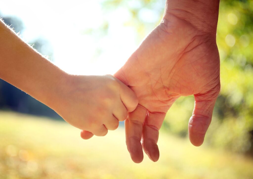 Child holding an adult's hand while walking outdoors.